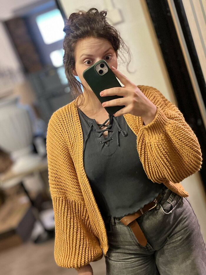 Woman taking a selfie wearing a handmade chunky crocheted mustard cardigan showcasing crochet project skills.