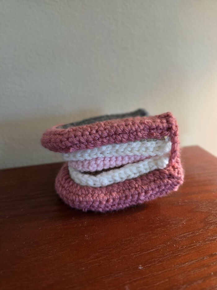 Crocheted small item with pink and white yarn, showcasing detailed stitch work in a compact design on a wooden surface.