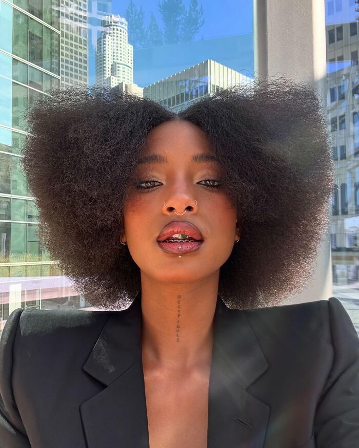 Young woman with large afro and piercings wearing a black blazer, showing entitled celebrity attitude about work and life.