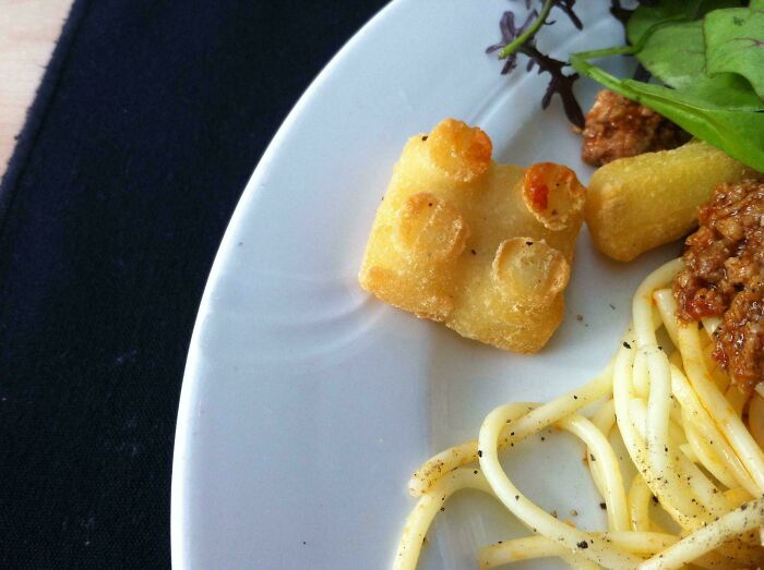 Close-up of a Danish prison cell-inspired Lego-shaped snack served with spaghetti and salad on a white plate.
