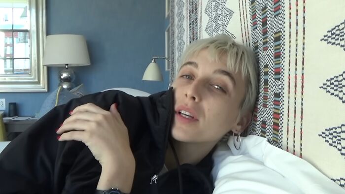 Young woman with short blonde hair in a black jacket reclining on a bed, reflecting on work and life entitlement.