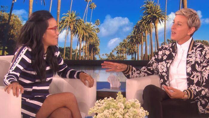 Two celebrities having a lively conversation about work and life on a daytime talk show set with palm trees backdrop.