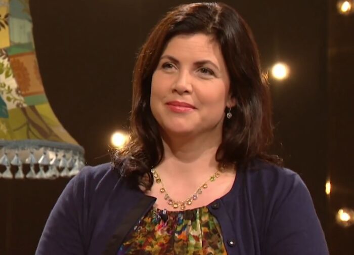 Woman with dark hair and floral top sitting in a studio setting, reflecting the theme of celebrities showing entitlement about work and life.