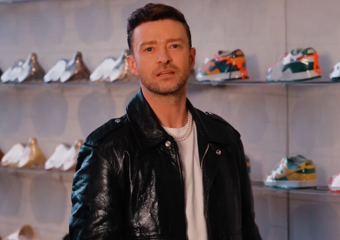 Man in a black leather jacket and pearl necklace standing in front of shelves with sneakers, showing celebrity entitlement.
