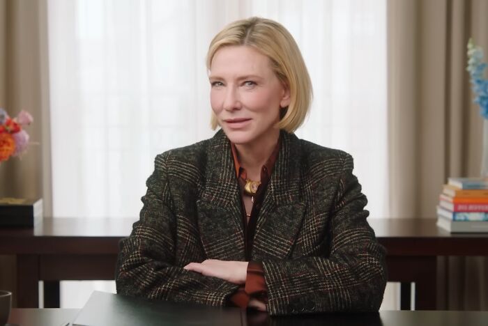 Woman with short blonde hair in a patterned blazer sitting at a desk, illustrating celebrities showing entitlement in work and life.