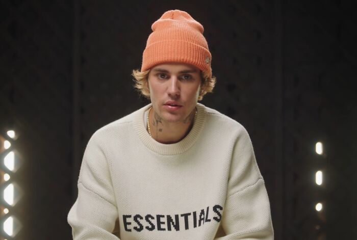 Young man wearing an orange beanie and essentials sweater, showcasing celebrity entitlement in work and life discussions.