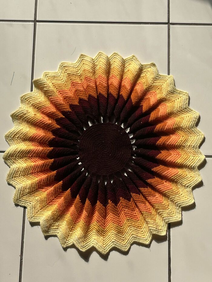 Crocheted circular pattern in warm gradient colors from dark brown to yellow displayed on white tiles.