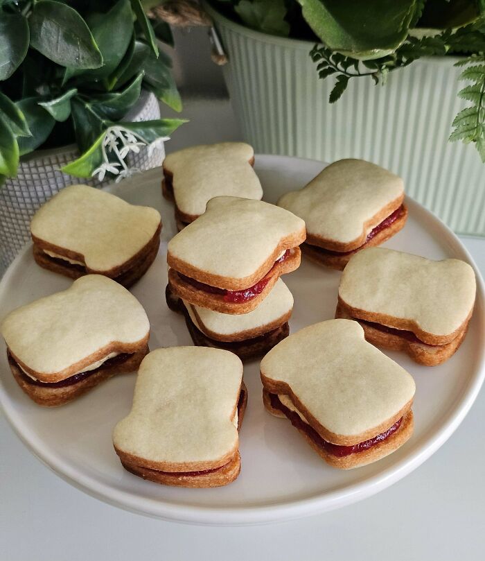 Stacked sandwich cookies with jam filling on a white plate, showcasing gorgeous baked goods with creative kitchen magic.