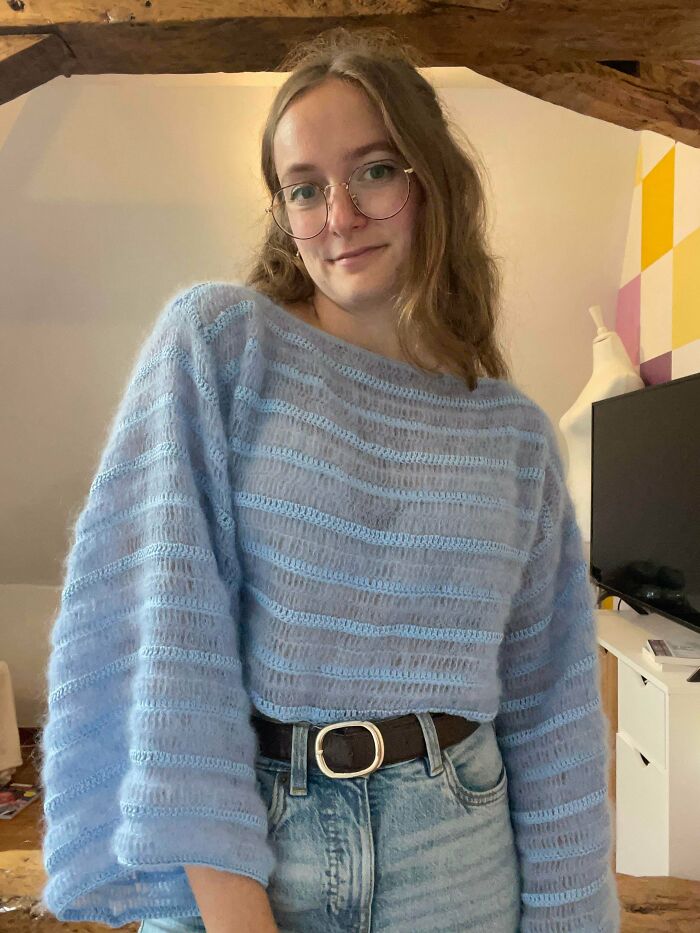 Young woman wearing a handmade light blue crocheted sweater, showcasing a beautiful crochet project indoors.