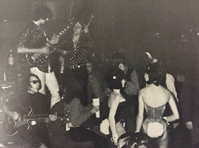 Black and white vintage photo showing a group of people playing music and socializing in a weird history scene.