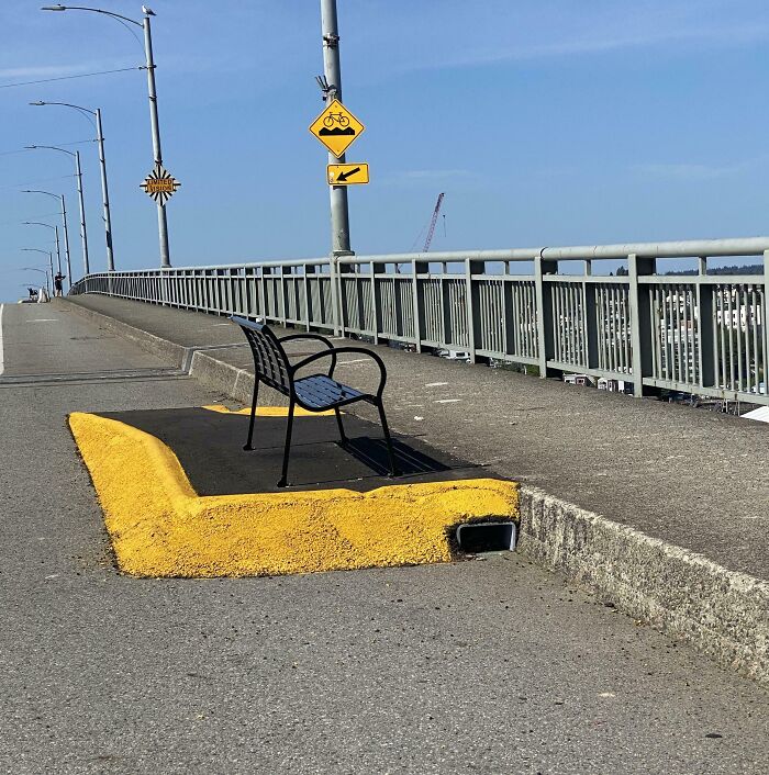 A bench installed on a raised curb on a bridge, showcasing a perfectly preventable fail in public seating design.