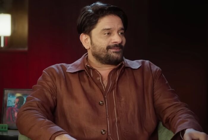 A man in a brown leather jacket sitting and smiling, illustrating celebrities showing entitlement about work and life.