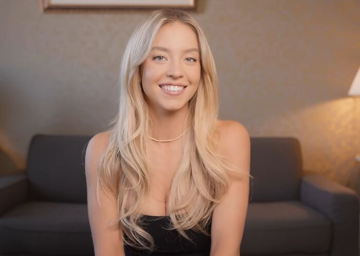 Young woman smiling indoors on a couch, illustrating celebrities showing entitlement while talking about work and life.