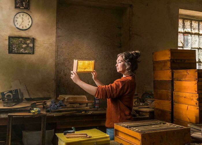 Woman examining translucent honeycomb in rustic room, capturing a moment resembling a Renaissance masterpiece.