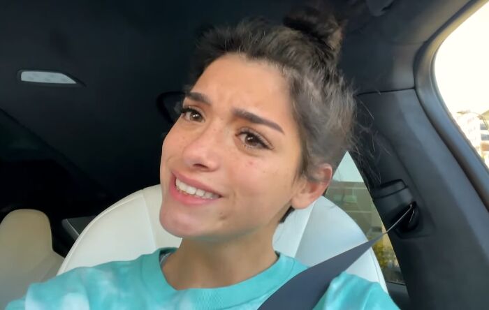 Young woman in a car wearing a blue shirt, expressing entitlement while talking about work and life.