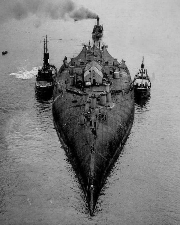 Extremely large things: A massive battleship, an extremely large and eerie vessel, being towed by smaller tugboats.