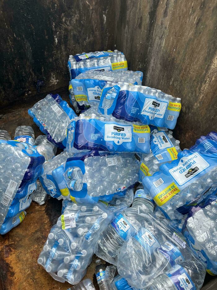 Several packs of purified drinking water bottles discarded in a dumpster diving treasures pile.