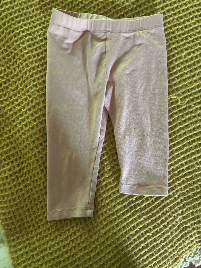 Light pink leggings with one leg shorter than the other, laid out on a textured green surface, moderately interesting clothing item.