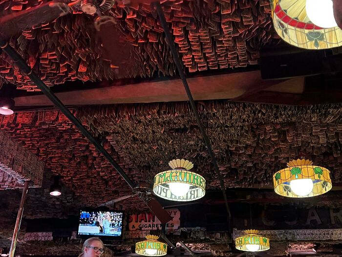 Bar ceiling covered with hanging dollar bills under stained glass pub lights in a moderately interesting setting.