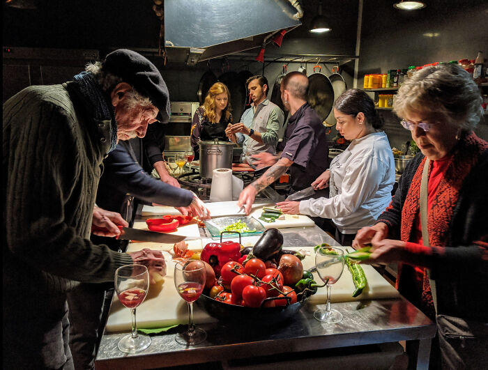 Group of people preparing food in a kitchen with vibrant vegetables, captured in an accidental renaissance photo style.