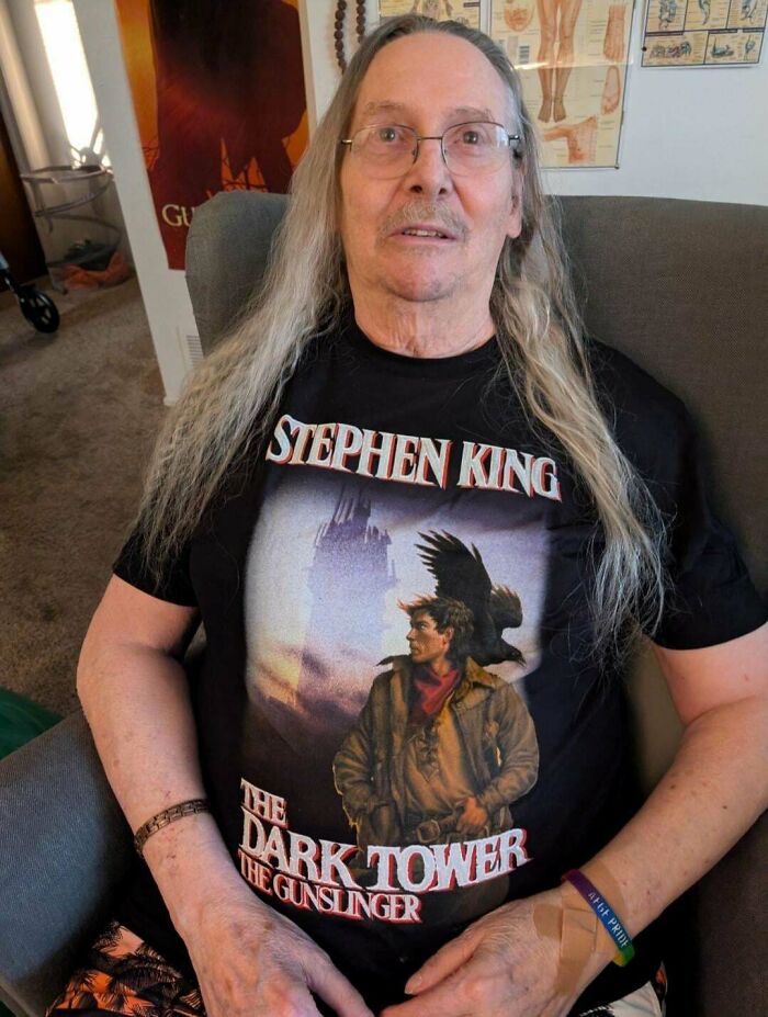 Older man with fierceflow beautiful hair men style wearing a Stephen King Dark Tower graphic t-shirt seated indoors.