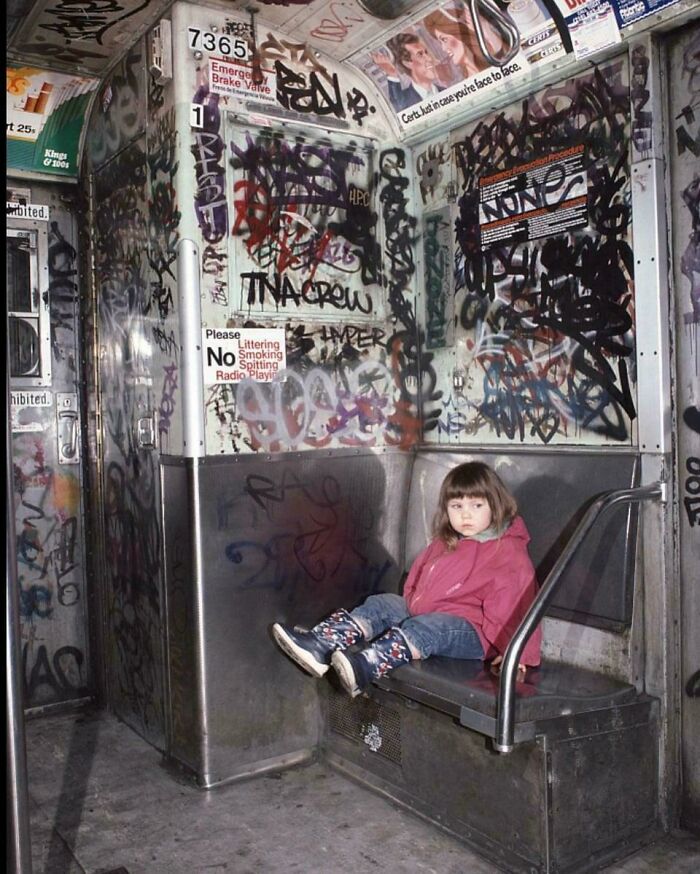 Young girl in a pink jacket sitting alone on a graffiti-covered subway seat, illustrating urban hell and societal decay.