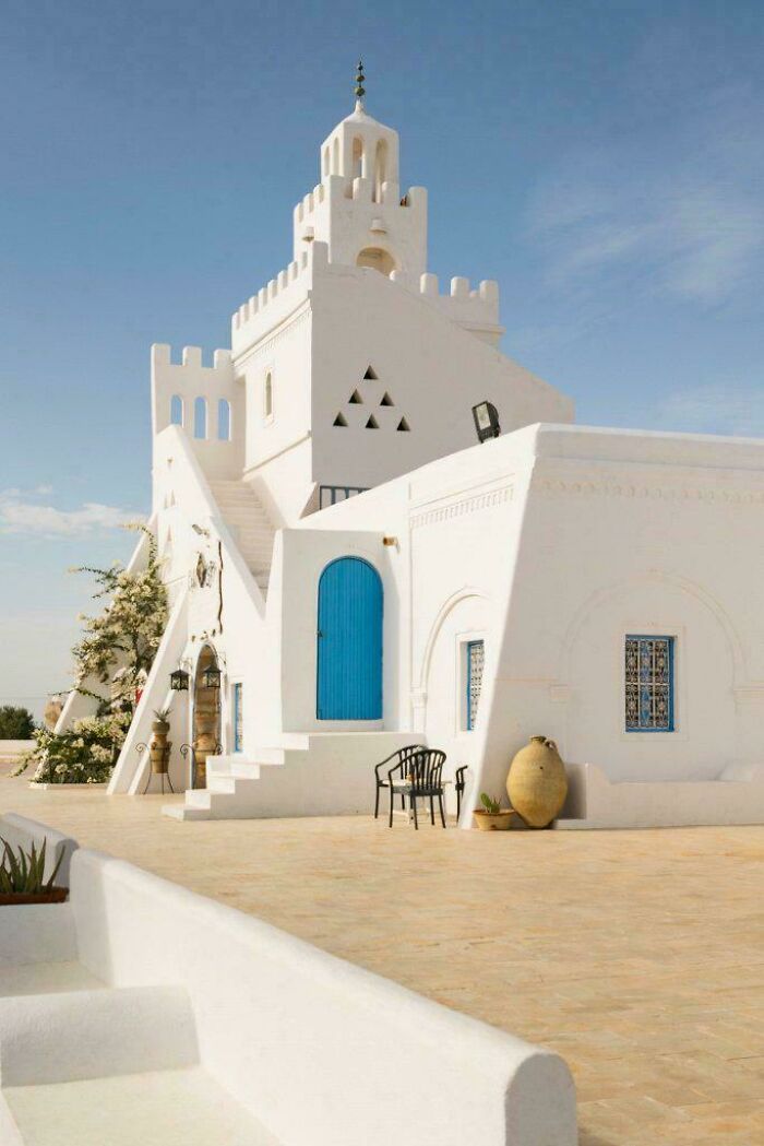 Stunning white building with a tower, blue doors, and minimalist architecture under a clear sky.