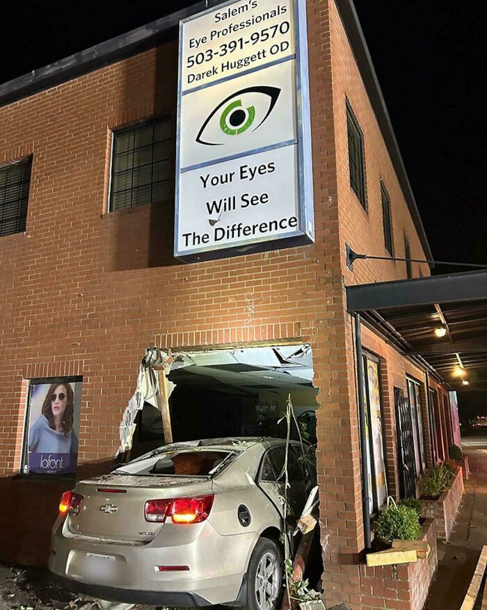 Car crashed into a brick building under an eye care sign, showcasing a humorous advertising placement fail.
