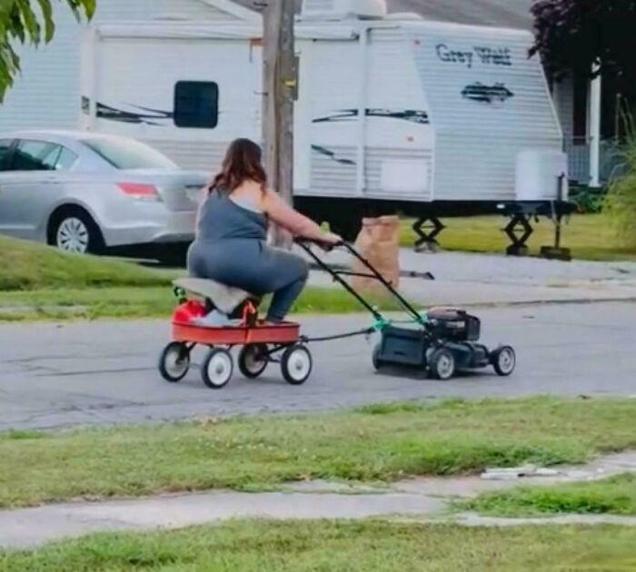 Woman riding a homemade wagon attached to a lawnmower showcasing redneck engineer ingenious creations outdoors.