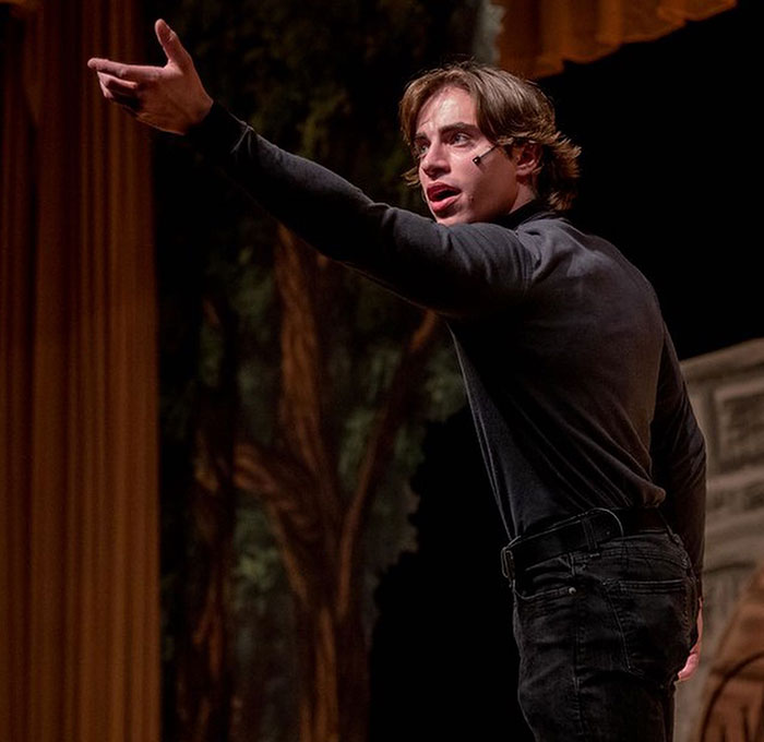 Young man performing on stage wearing a headset microphone, representing Chase Filandro in a dramatic scene.