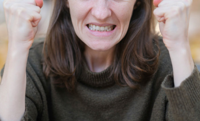Frustrated woman clenching fists indoors, expressing anger related to roommates refusing to give back AC unit.