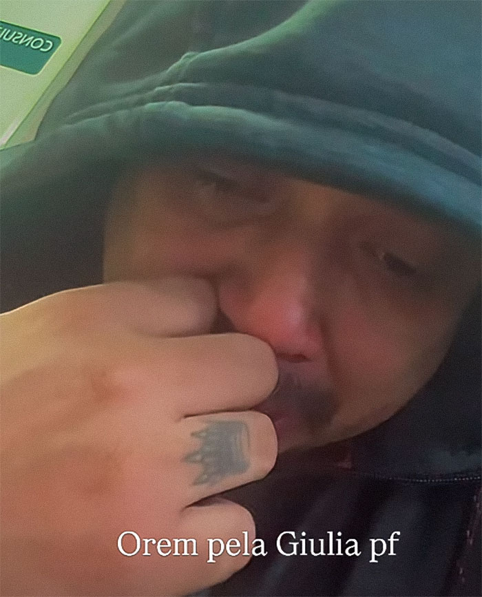 Man in a hooded jacket with a tattoo on his hand, appearing emotional, related to a 2-year-old drowning incident.