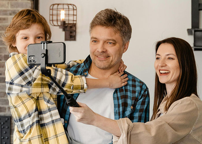Family taking a selfie with a smartphone, smiling together while capturing moments and enjoying time indoors.
