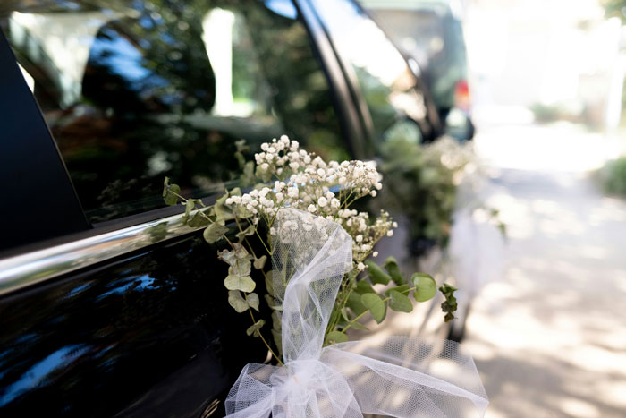 Close up of wedding car decorated with white flowers and tulle, illustrating unhinged wedding spends shared by people. - 40