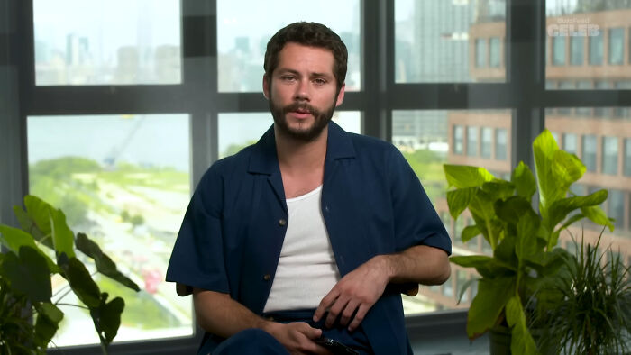 Actor in a casual outfit sitting by the window, featured in a discussion about Hollywood celebrities and leading A-listers.
