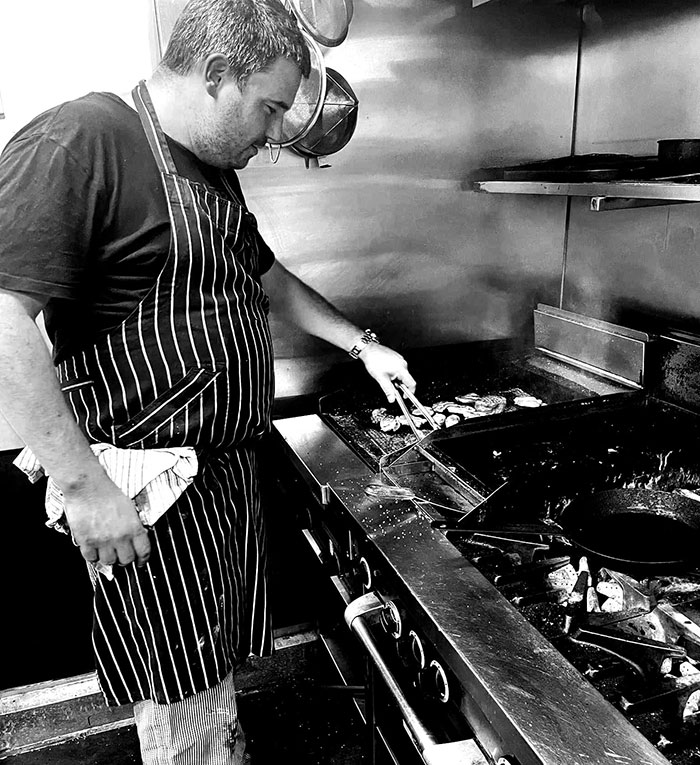 Caf&eacute; owner cooking at grill, addressing entitled customers after teen worker was left in tears at the caf&eacute;.