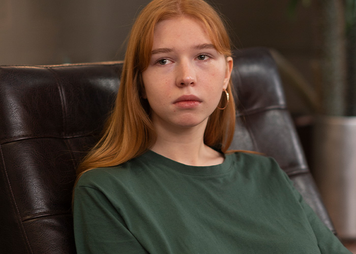 Young woman in a green shirt sitting on a leather chair, looking thoughtful about house fires caused by Roomba accidents.