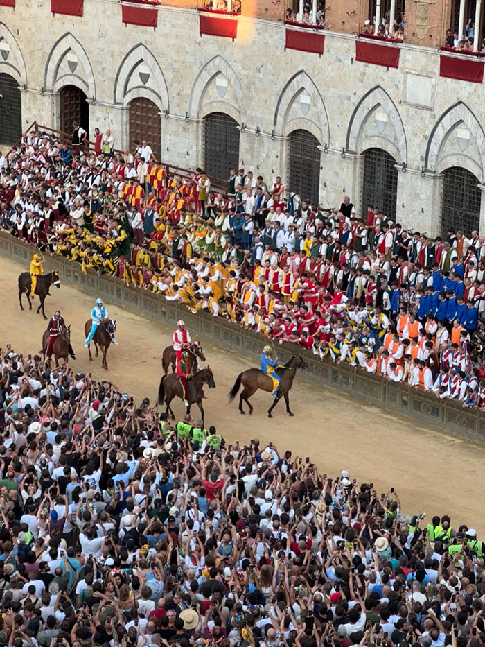 Crowd at an outdoor event, with spectators watching horse riders and participants in colorful traditional costumes.