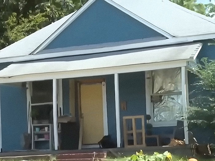 Blue house exterior with porch and open door, related to stepdad and mom felony charges after home childbirth by 11-year-old.