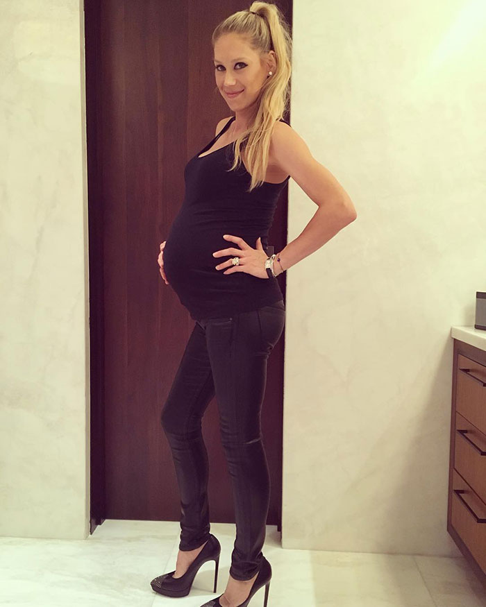 Anna Kournikova with a visible pregnancy bump, wearing black outfit and heels, posing indoors for announcement. Anna Kournikova with a visible pregnancy bump, wearing black outfit and heels, posing indoors for announcement.
