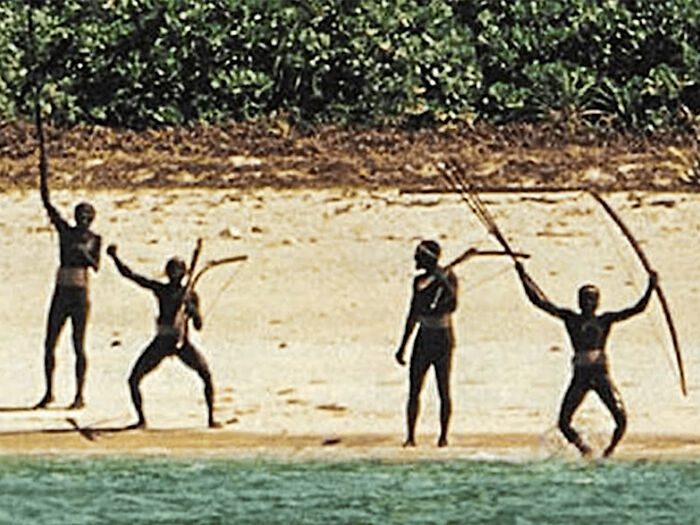 Indigenous tribe standing on a beach holding bows and arrows, highlighting controversy over influencer's viral TikTok filming stunt.