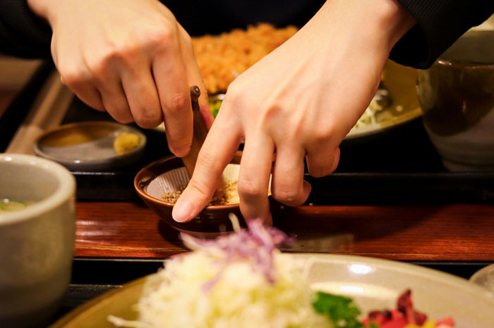 Hands grabbing food with chopsticks at a table, illustrating a woman sick of her coworker helping herself to food.