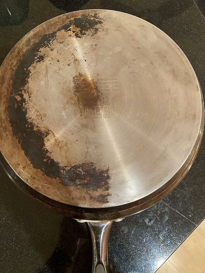 Bottom view of a stainless steel pan showing burned stains, a common daily annoyance in kitchen cookware.