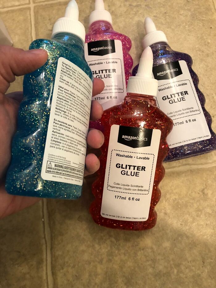 Bottles of colorful glitter glue held and placed on a floor, ideal back to school finds for creative projects.