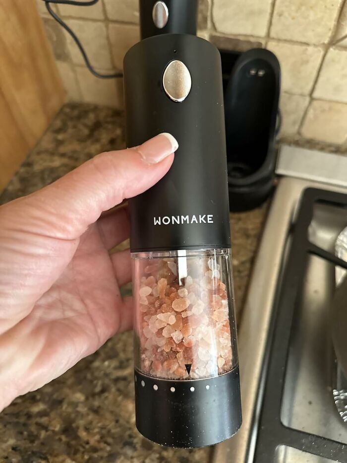 Hand holding a smart kitchen tool electric salt grinder with Himalayan salt inside on a kitchen counter.