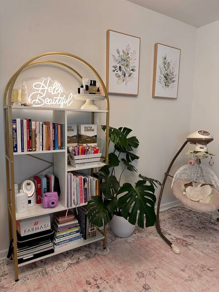 White and gold decorative shelving unit with books, skincare, and a plant in a cozy room featuring useful decor items.