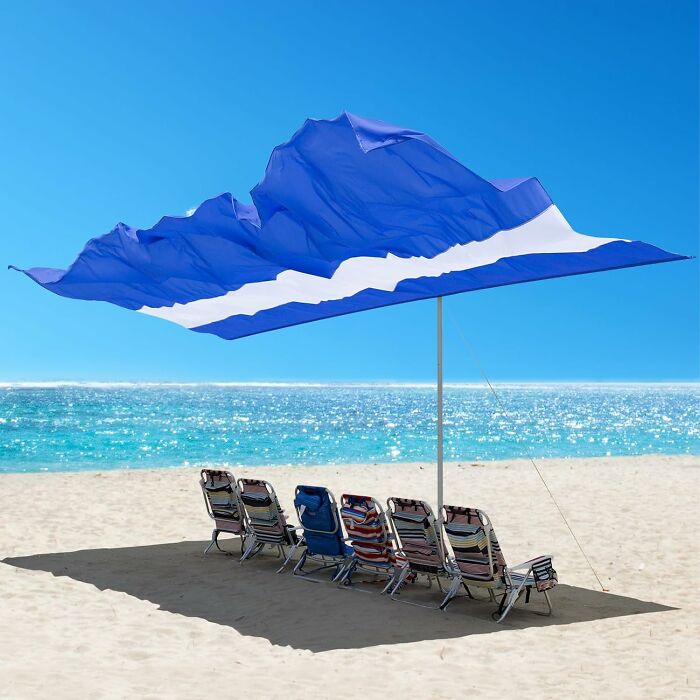 Beach chairs under a large blue sunshade on a sandy beach, illustrating heatwave hacks for staying cool.