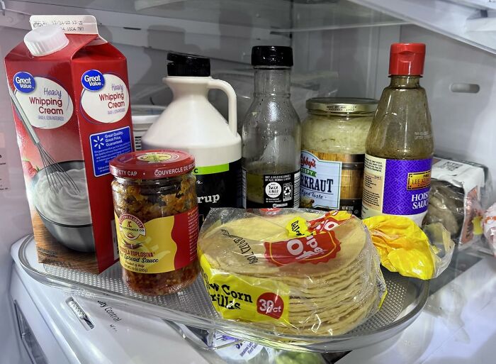 Fridge shelf with heavy whipping cream, syrup, hot sauce, horseradish, and a pack of corn tortillas in an organized Amazon finds setup.