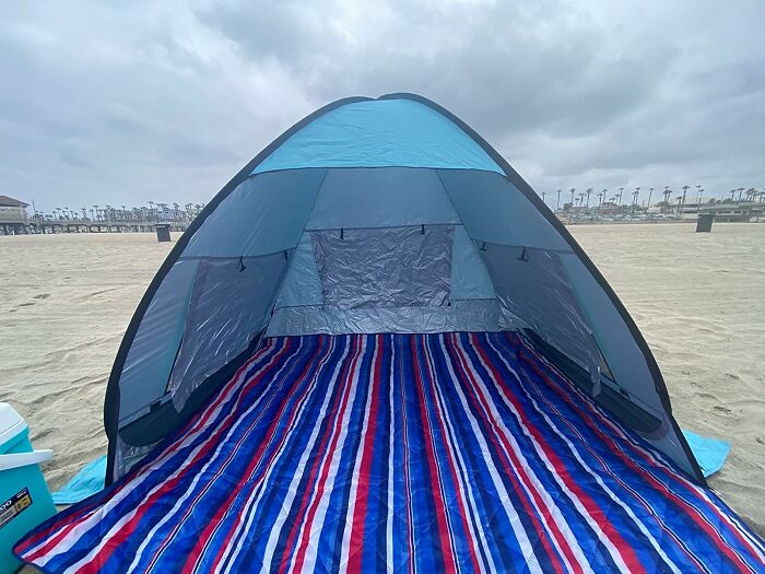Beach tent with striped mat set up on sand under cloudy sky as part of heatwave hacks for summer comfort.