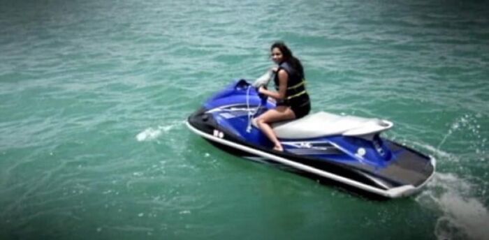 Woman riding a blue jet ski on clear green water, captured in an unsettling image from the morbid knowledge group.